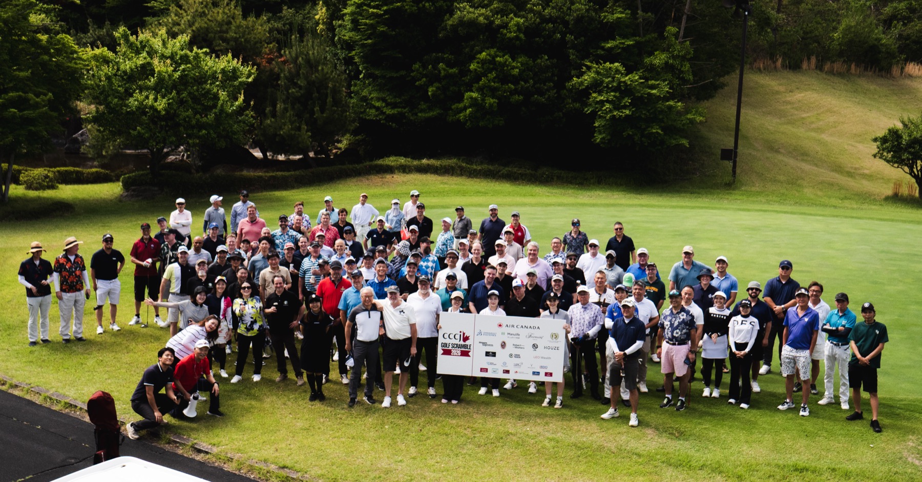 The full field of golfers assembled on the fairway behind the tournament board