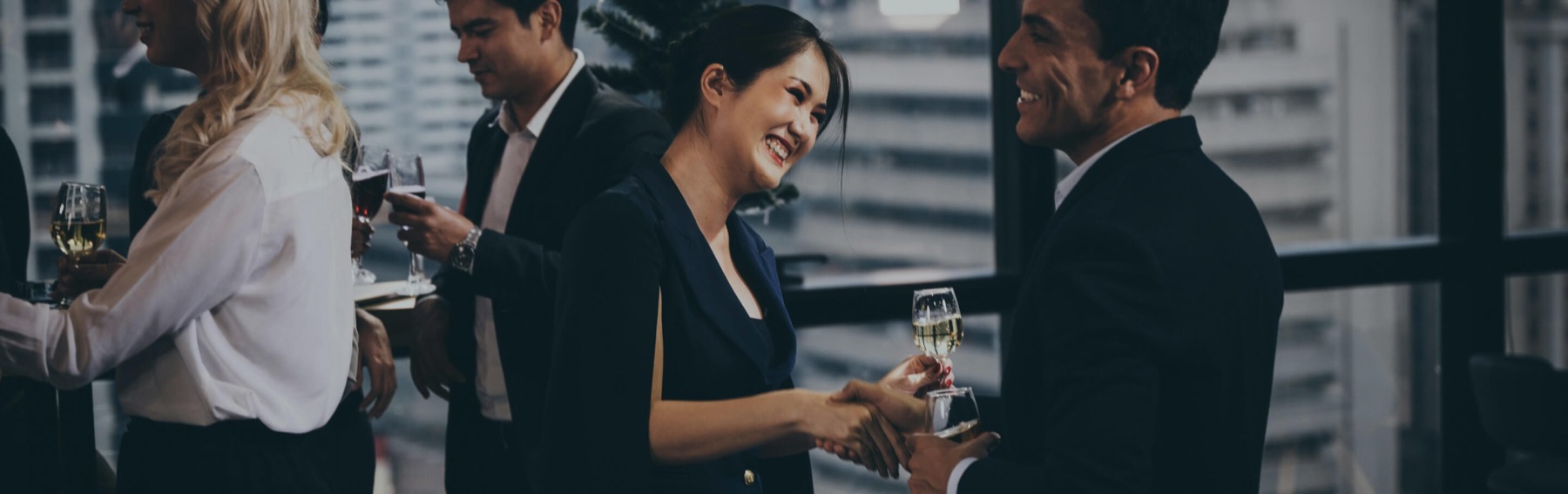 Guests in conversation over drinks beside a window above the city